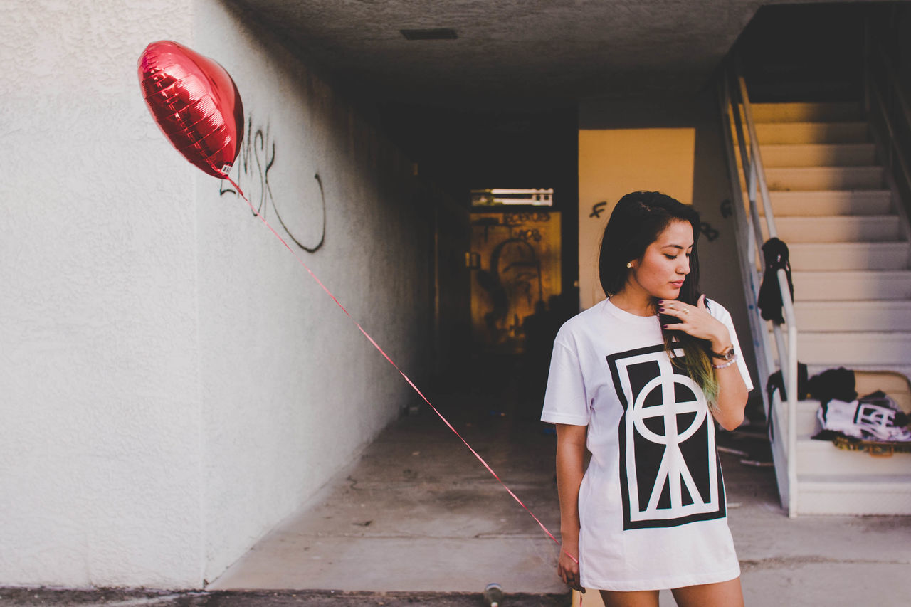 YOUNG WOMAN STANDING AGAINST WALL IN BUILDING