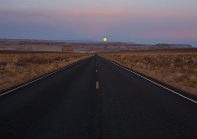 Empty road along landscape at sunset