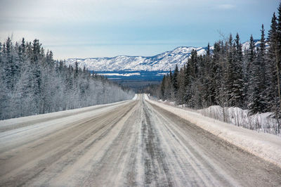 Snow covered road by mountain against sky