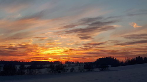 Scenic view of snow covered landscape against orange sky