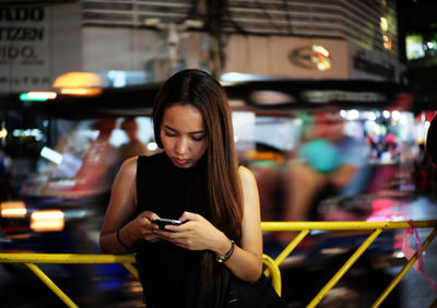 Young woman using mobile phone while standing by railing