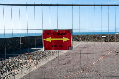 Information sign on wall by fence against sky