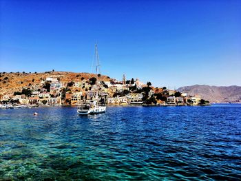 Sailboats in sea by townscape against clear blue sky