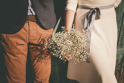 Midsection of bride and bridegroom with bouquet during wedding ceremony