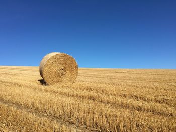 Hay bale on field against clear blue sky