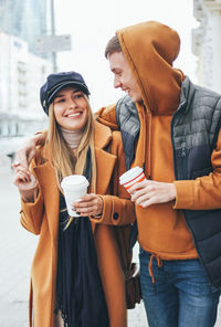 Smiling young couple holding disposable cups while walking in city