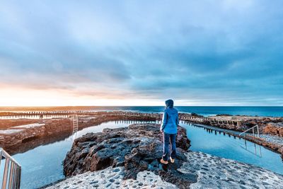 Rear view of woman standing by sea against sky