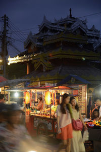 People by illuminated market stall at night