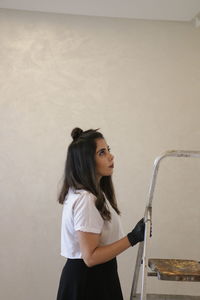 Side view of young woman standing against wall