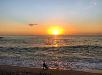 Silhouette man standing on beach against orange sky