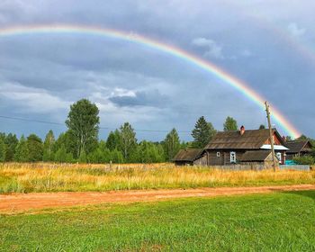 Scenic view of rainbow over field and houses against sky