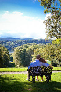 Rear view of couple sitting on landscape against sky