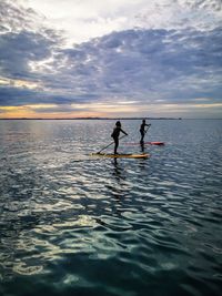 People on sea against sky during sunset