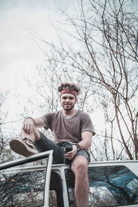 Low angle portrait of young man sitting on car roof