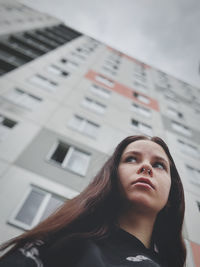 Portrait of young woman standing against building