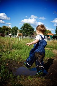 Full length of boy splashing mud on field against sky