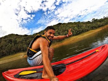 Portrait of young man gesturing peace sign on kayak in lake