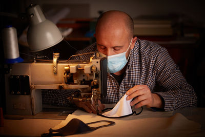 Man sewing mask with machine on table