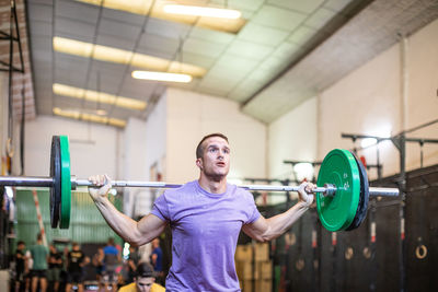 Muscular guy lifting barbell in modern gym