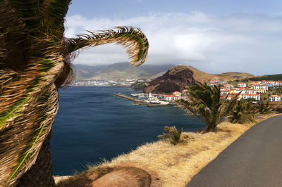 Distant view of camara de lobos by sea against cloudy sky