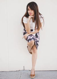 Full length of young woman standing on one leg against white wall