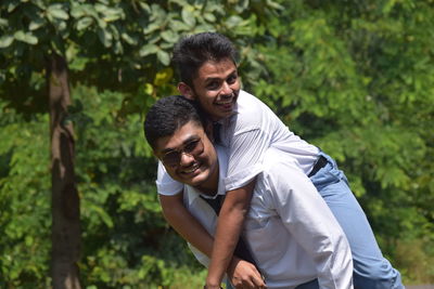 Portrait of happy man piggybacking friend against trees