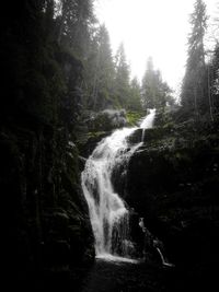 Waterfall in forest against sky