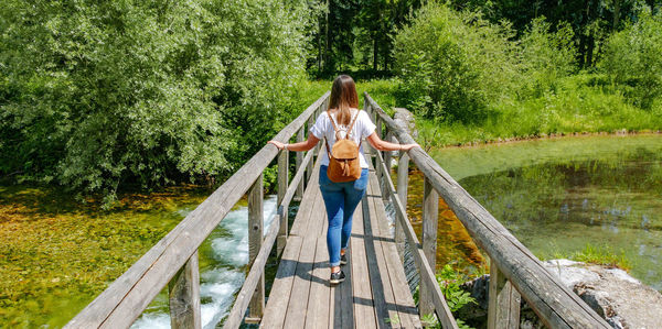 Rear view of young woman standing on footbridge over creek.