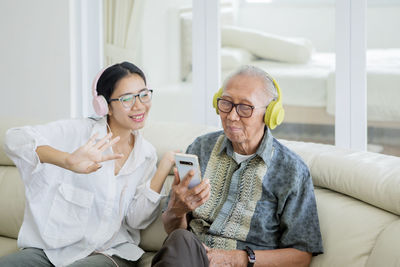 Happy woman and grandfather watching video in phone while sitting on sofa