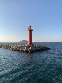 Lighthouse amidst sea and buildings against clear sky