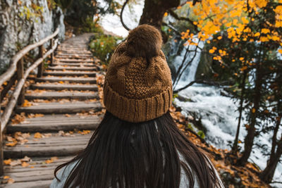 Rear view of young adult woman walking on wooden path in forest in autumn.