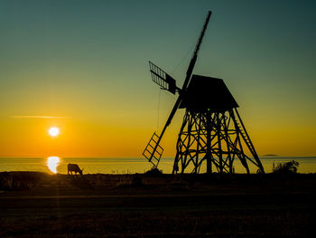 Silhouette windmill on land against sky during sunset