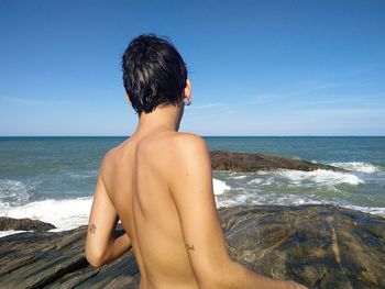 Rear view of shirtless man on beach against sky