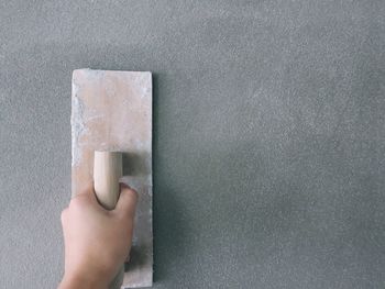 Close-up of worker using scrapper on gray wall at construction site