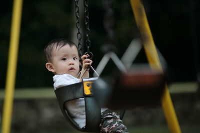 Side view portrait of boy sitting on swing at playground