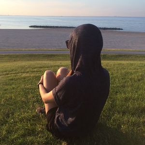 Rear view of woman sitting on land by sea against sky