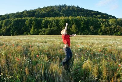 Rear view of woman standing on field against trees