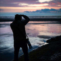 Woman photographing sea against sky during sunset