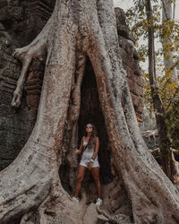 Portrait of young woman standing by tree trunk