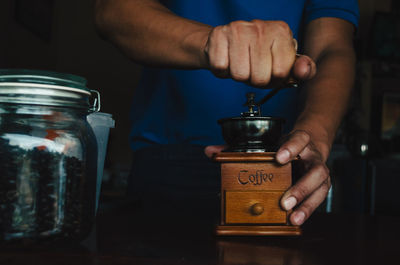 Midsection of man grinding beans in coffee grinder on table