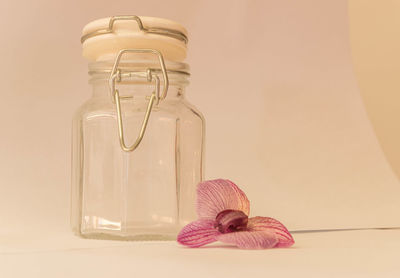 Close-up of glass jar on table with flower against wall