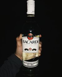 Close-up of hand holding bottle against black background