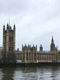Houses of parliament at waterfront against cloudy sky