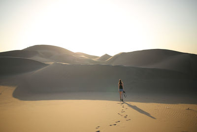 Man on sand dune in desert against sky