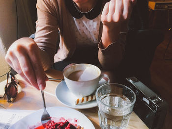 Midsection of woman holding drink sitting on table