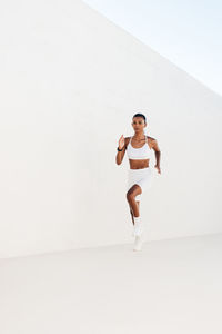 Full length of young woman jumping against white background