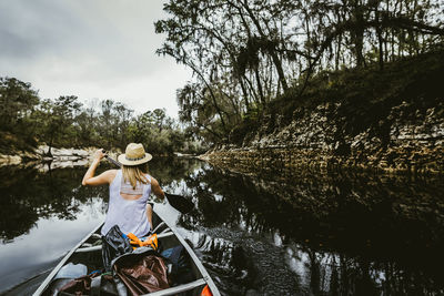 Rear view of young woman rowing canoe with oar in lake at forest