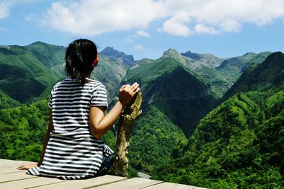 Rear view of woman looking at mountains while sitting on observation point