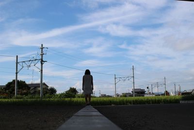 Rear view of woman standing on footpath over field against sky