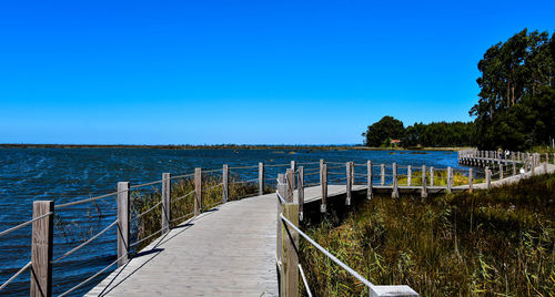 Footpath by sea against clear blue sky